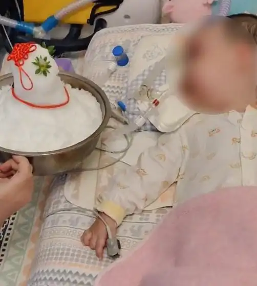 女儿患病卧床治疗,妈妈堆小雪人用盆端病床前她看下雪很认真

